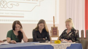 Uczennica oraz nauczyciele za stołem podczas czytania